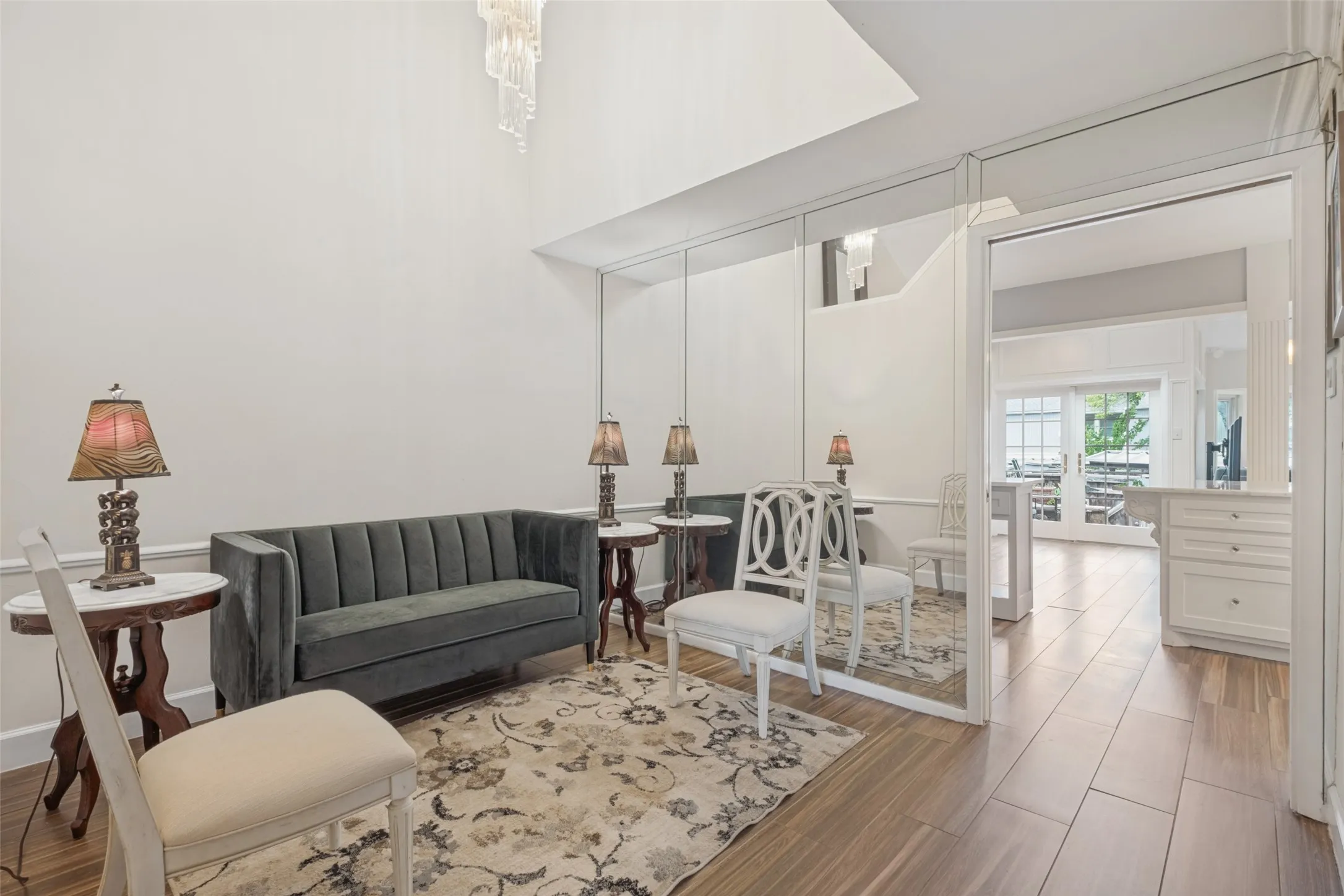 High ceilings with a decorative chandelier, wood-finish flooring throughout, and mirrored wall panels