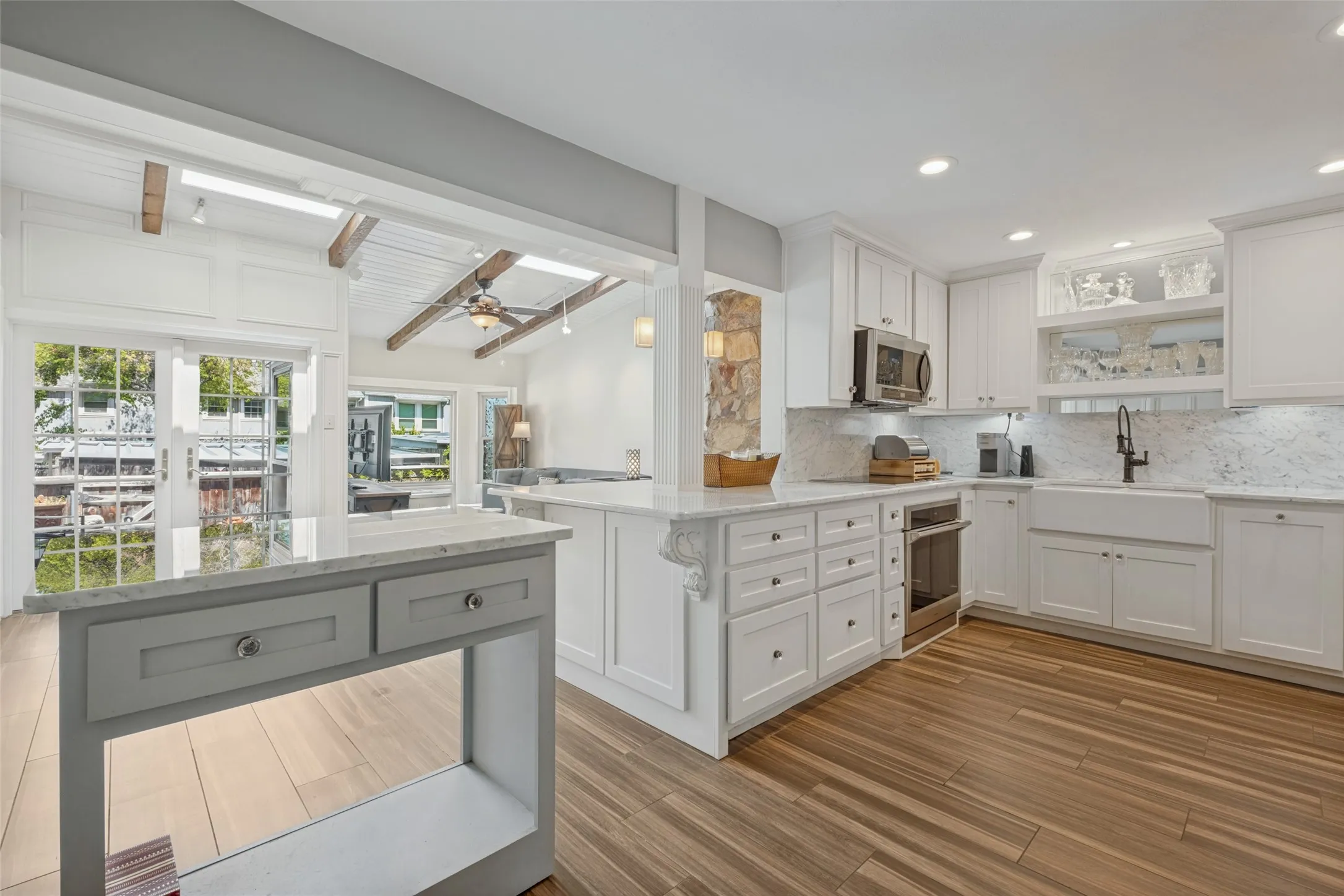 White cabinetry kitchen with wood-finish flooring, undermount sink, stainless steel appliances, and stone accent column