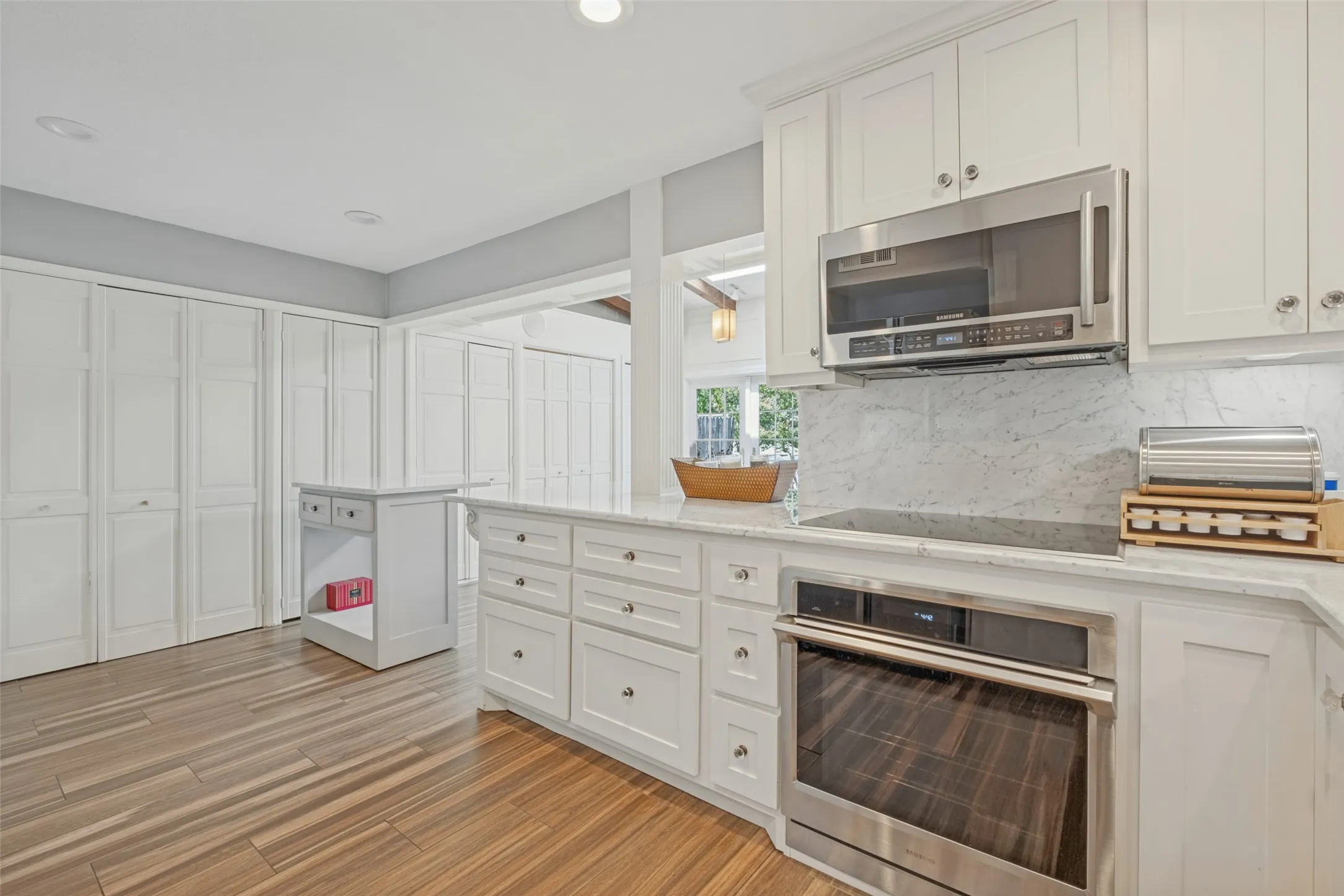 Bright kitchen with white cabinetry, stainless steel appliances, wood-finish flooring, and a stone backsplash