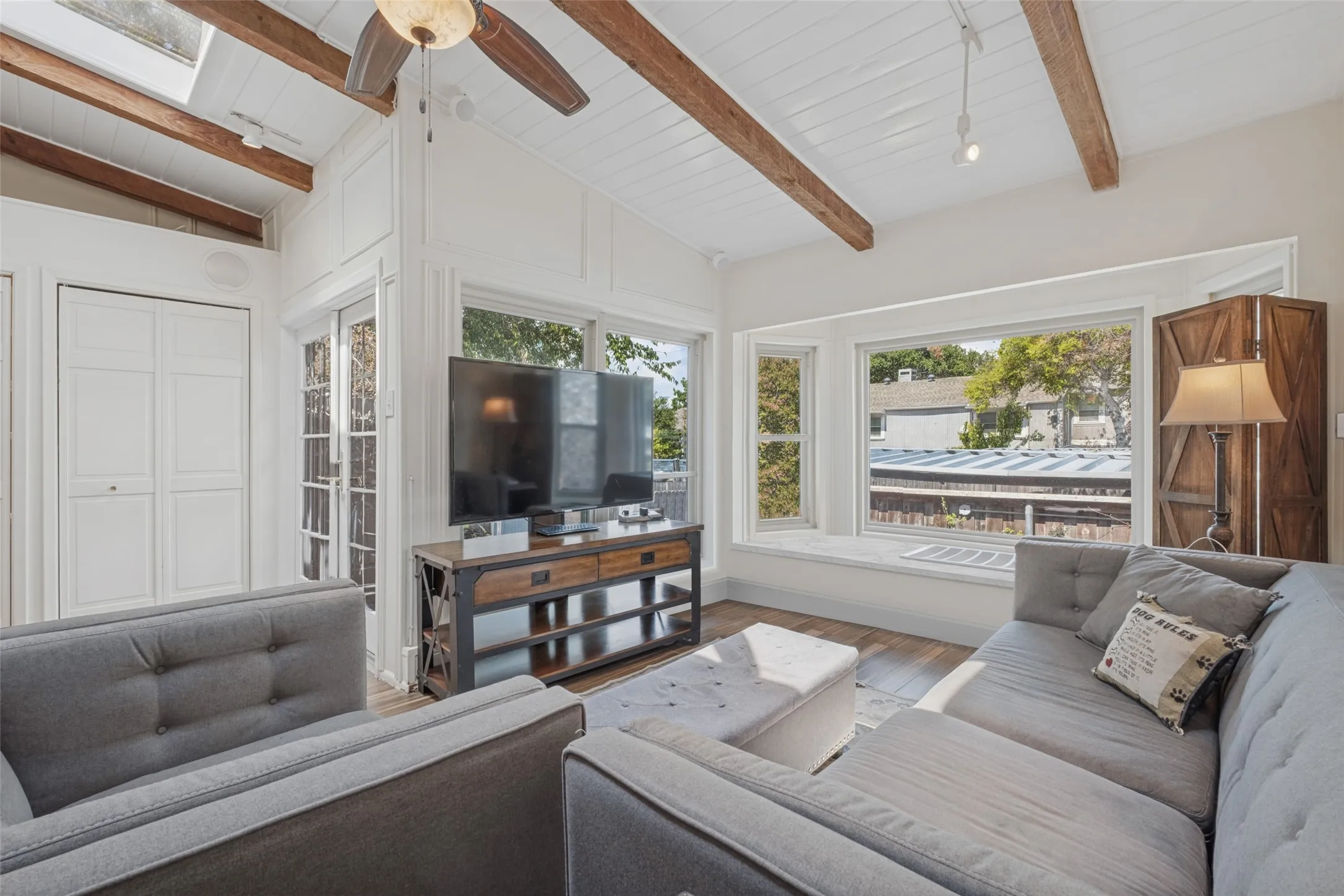 Vaulted ceiling with exposed wood beams, wood-finish flooring, multiple windows, and French doors