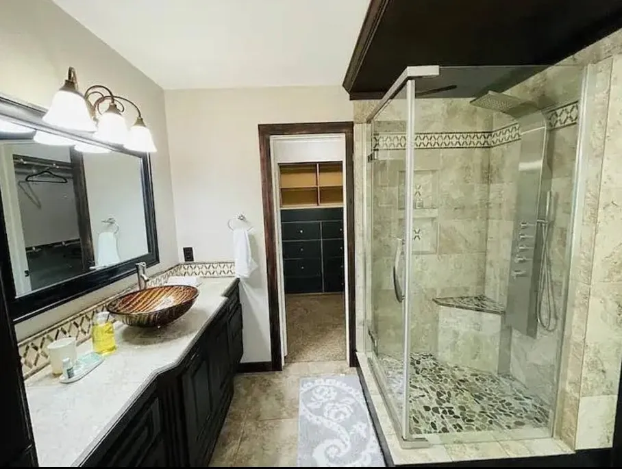Custom vessel sink with an extensive vanity, fully-tiled shower with a built-in bench, shower panel system, and glass enclosure, and an adjacent walk-in closet