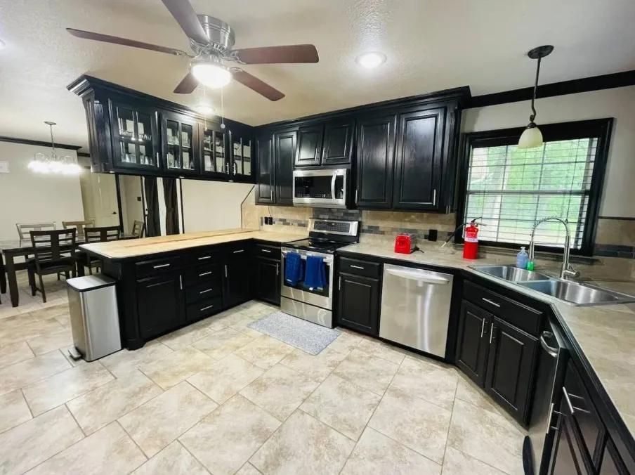 Spacious kitchen featuring dark wood cabinetry, stainless steel appliances, light-toned countertops, tile flooring, and a ceiling fan with integrated lighting
