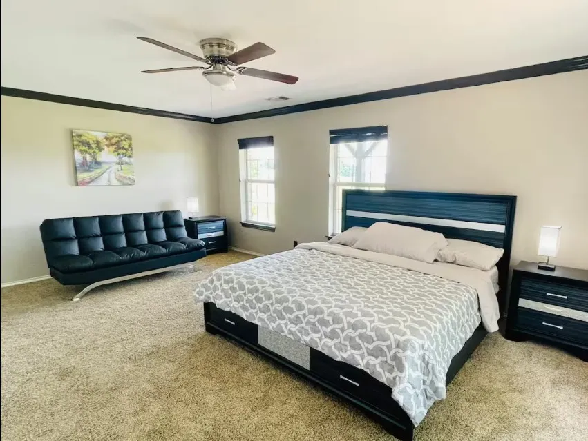 Neutral tone wall paint, dark crown molding, carpeted flooring, two windows, and a ceiling fan with integrated lighting