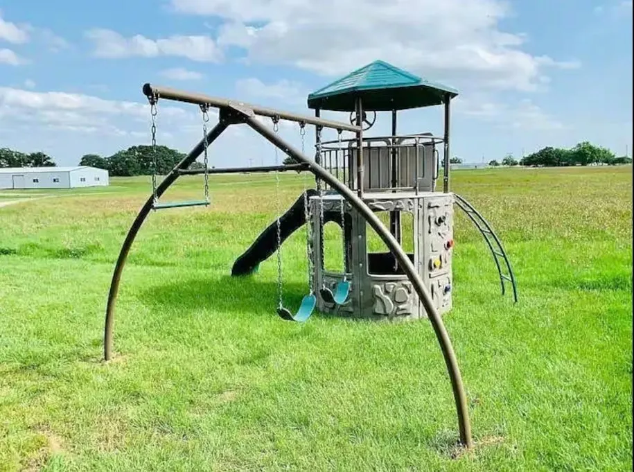 Expansive grassy area featuring a built-in playset with swings, slide, and climbing wall