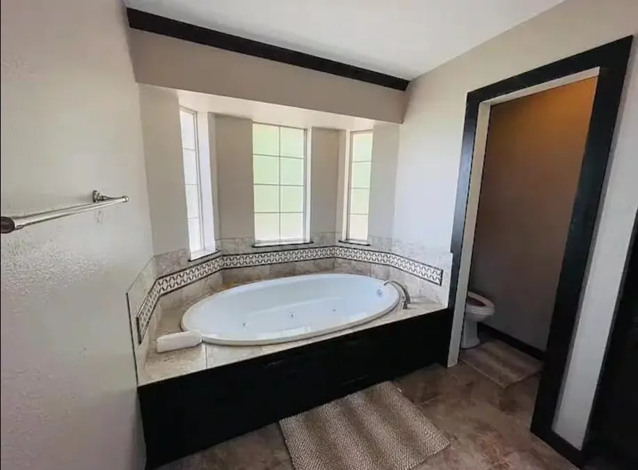Oval soaking tub with tiled surround, bay windows, and mosaic accent tile