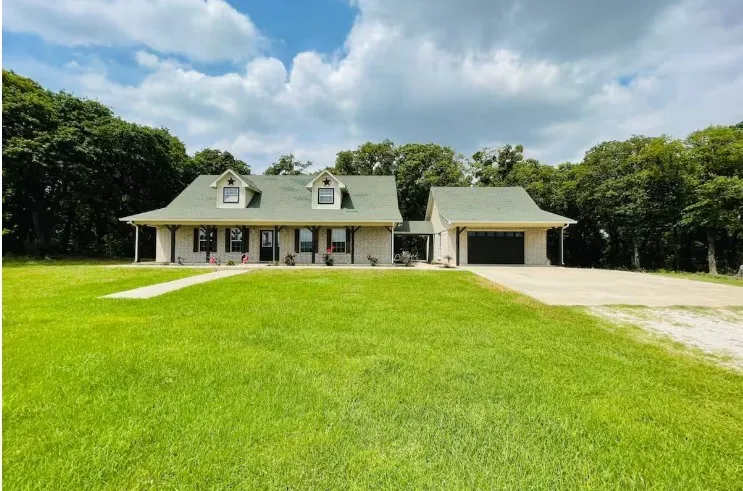 Gabled roofline with dormer windows, covered front porch, attached garage, concrete driveway, and a expansive front lawn