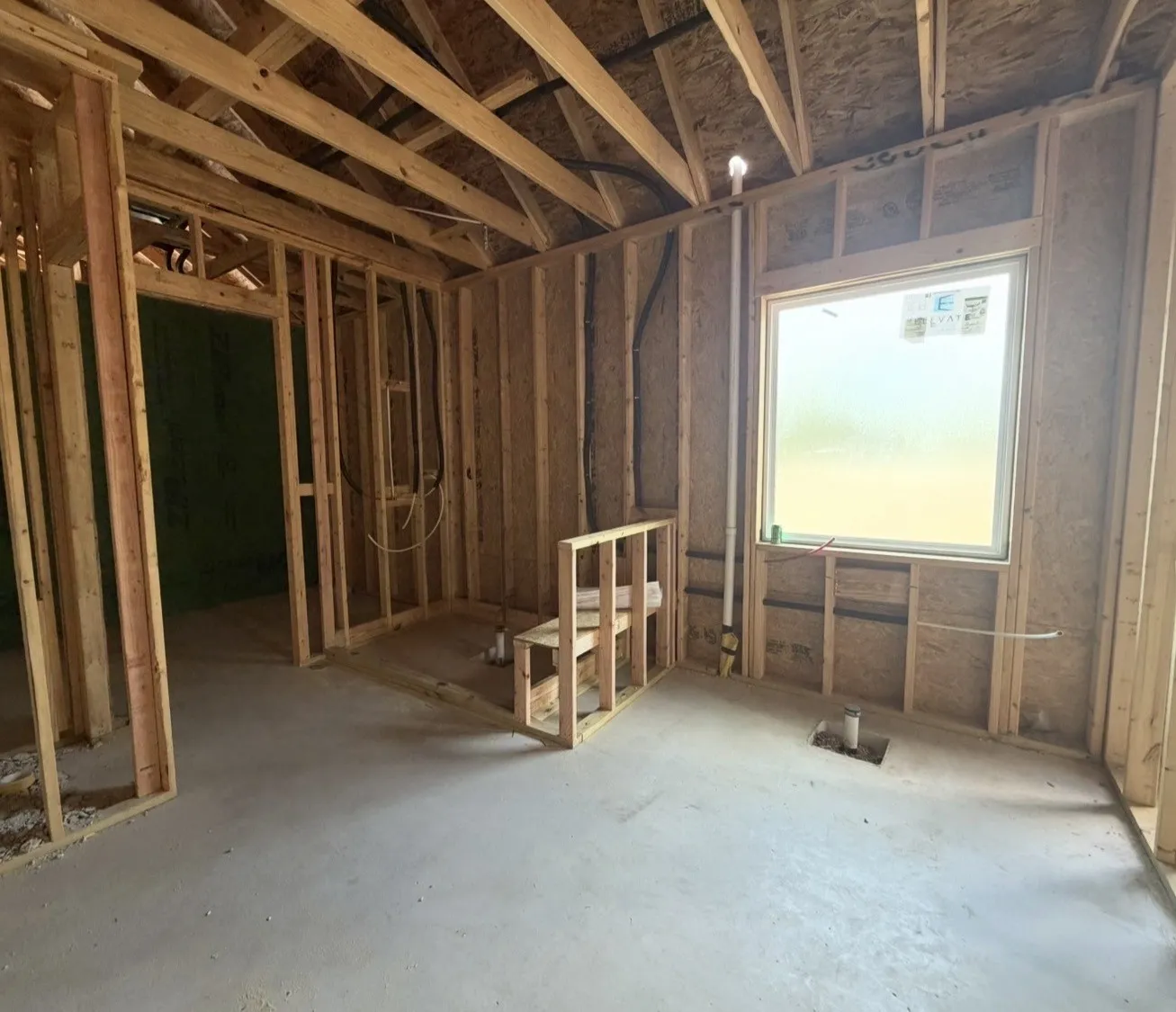 Interior framing showcasing structural elements, a framed window opening, and a concrete floor