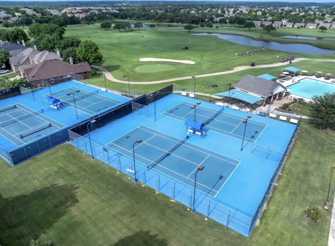 Multiple tennis courts with blue surfacing, surrounded by green landscaping