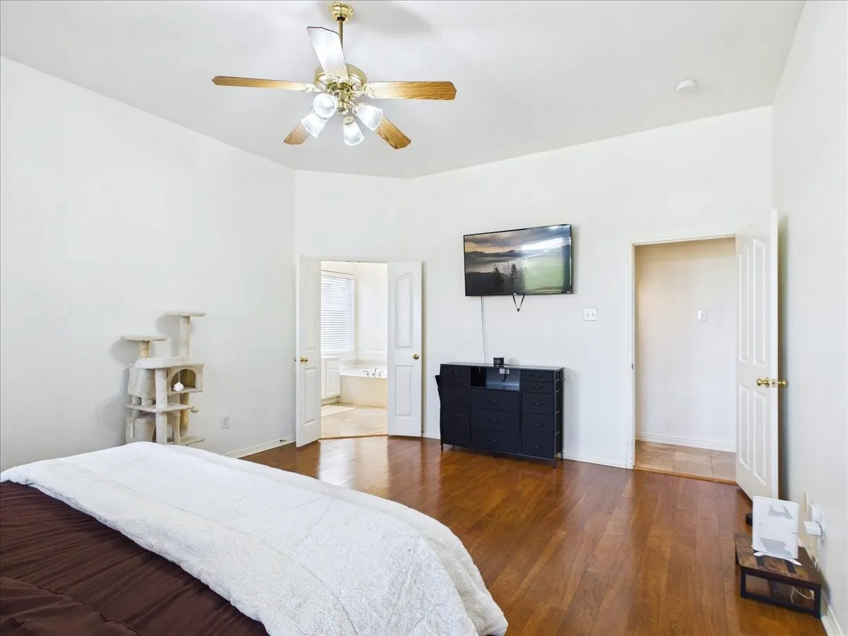 Spacious primary bedroom featuring gleaming wood-finish flooring, recessed ceiling lighting, and a ceiling fan with integrated light fixture