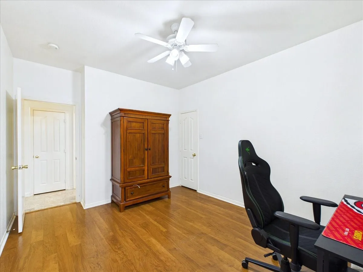 Spacious bedroom showcasing refinished wood flooring, ceiling fan with integrated lighting, and abundant natural light