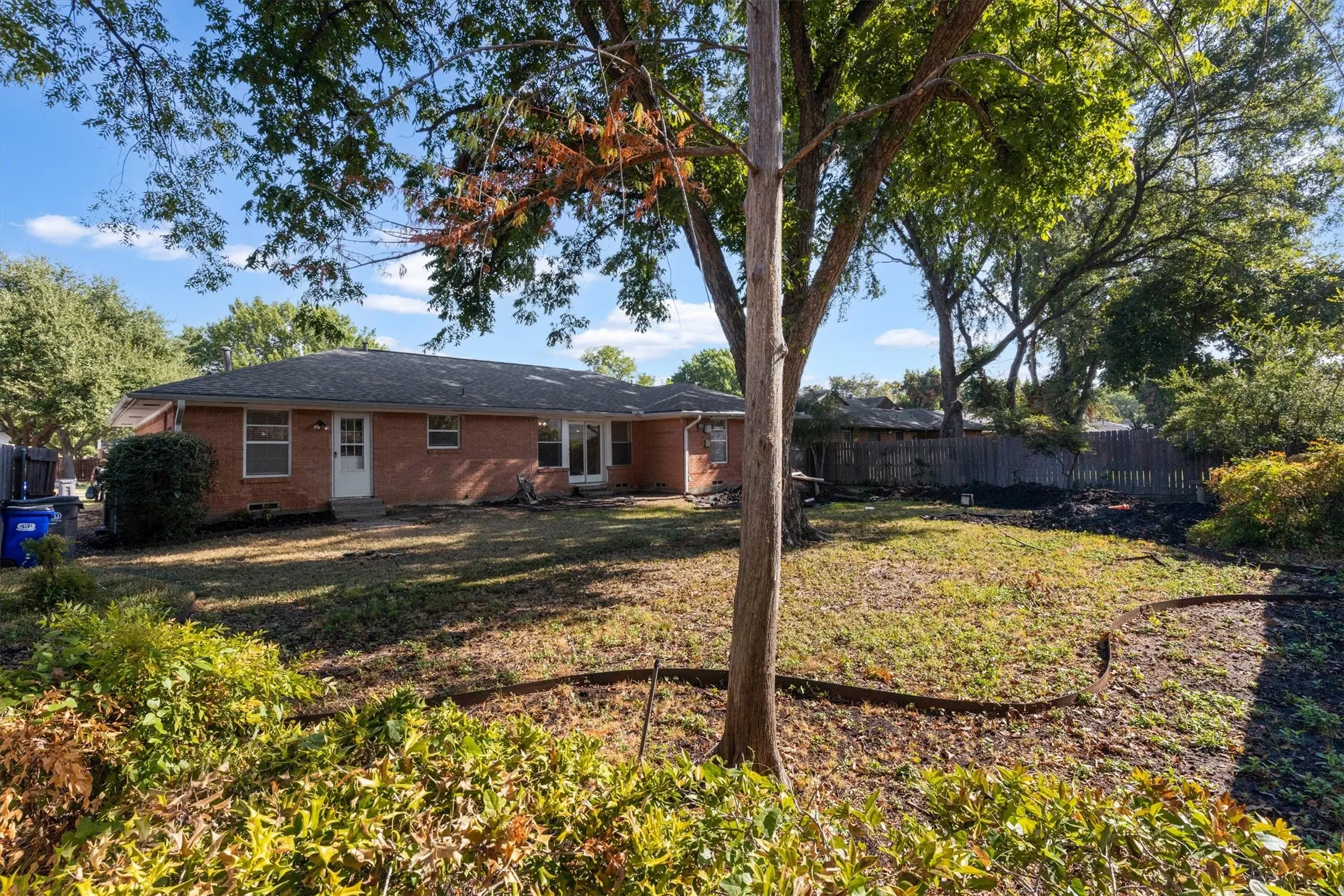 Expansive backyard with a manicured lawn, mature trees, and a wooden privacy fence