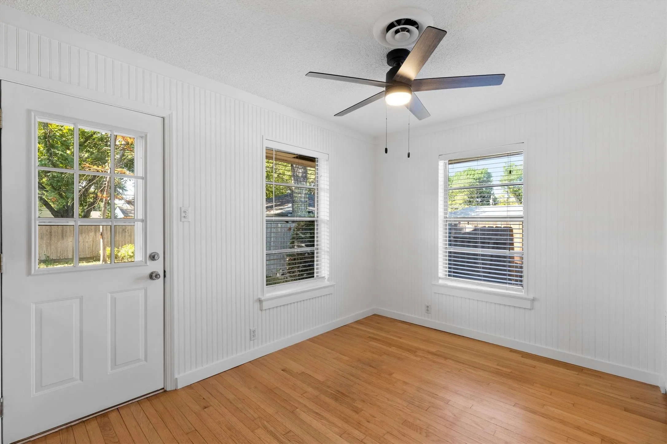Wood-finish flooring, white beadboard wall paneling, and an exterior access door with divided lites