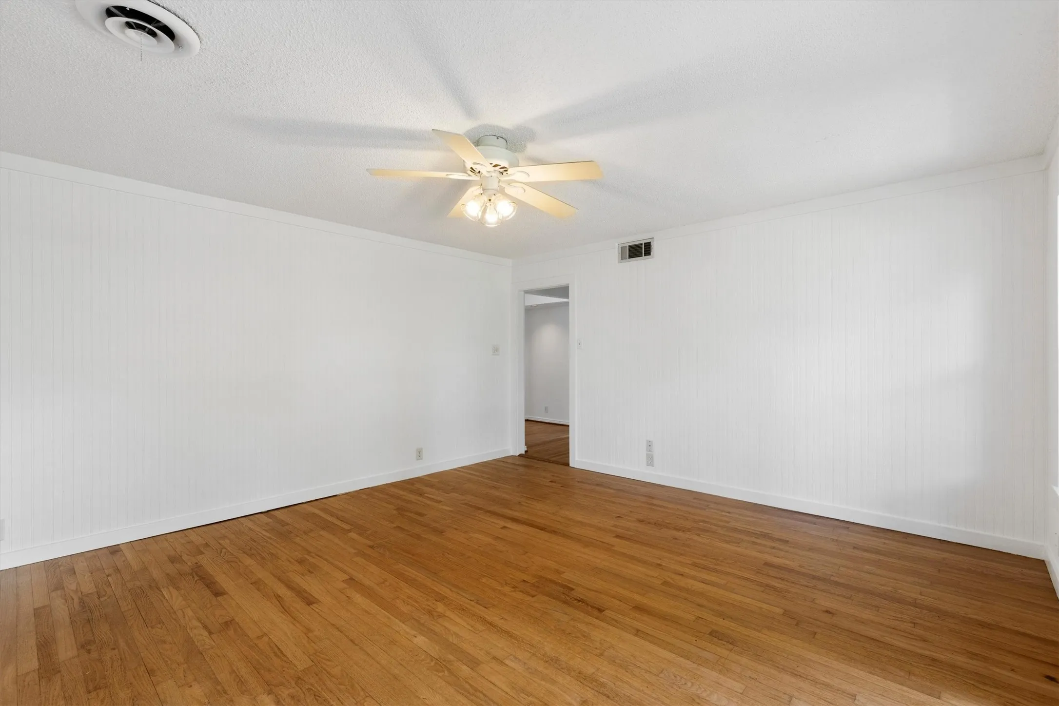 Wood-finish flooring with white paneled walls and a ceiling fan with integrated lighting