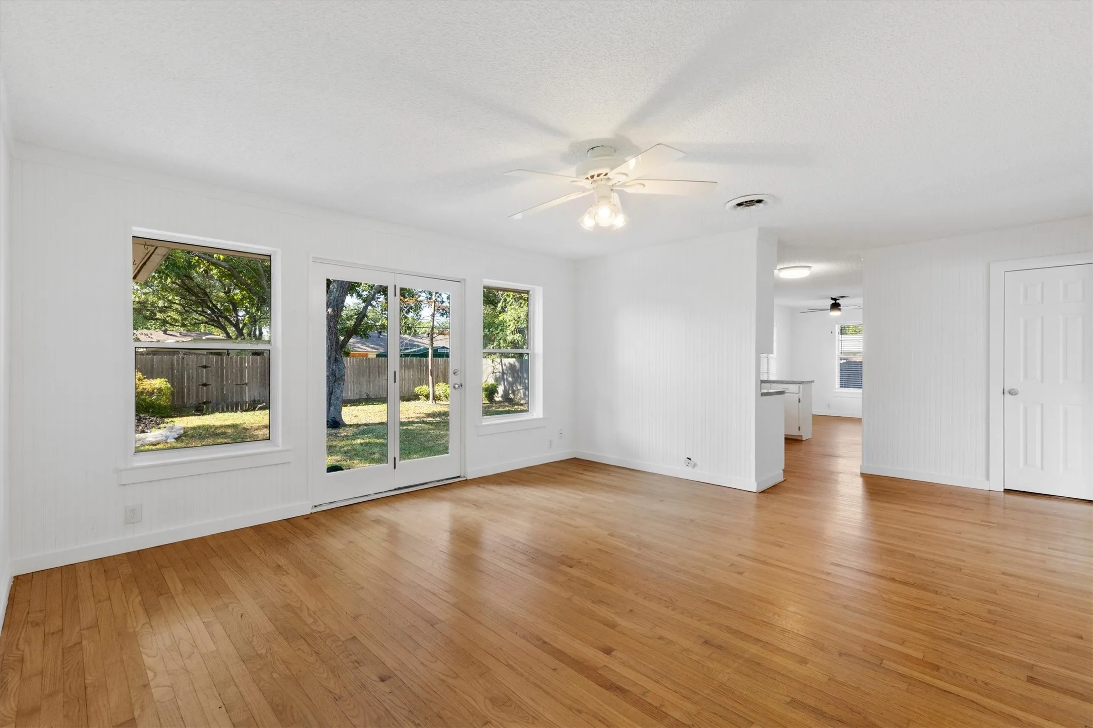 Hardwood flooring, white walls, ceiling fan, white trim, and a glass-paneled door