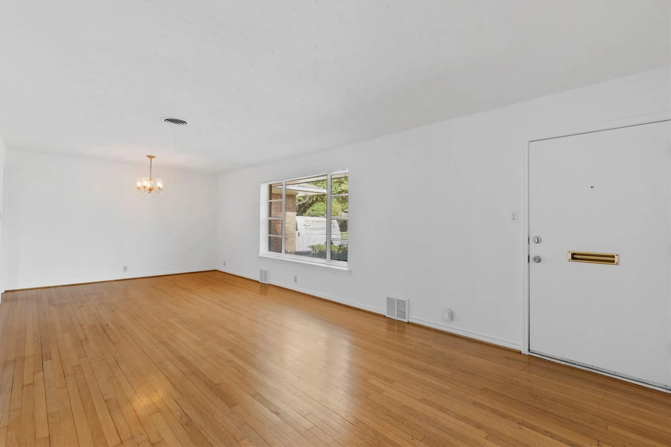 Wood-finish flooring, a crystal chandelier, and a large window with exterior views