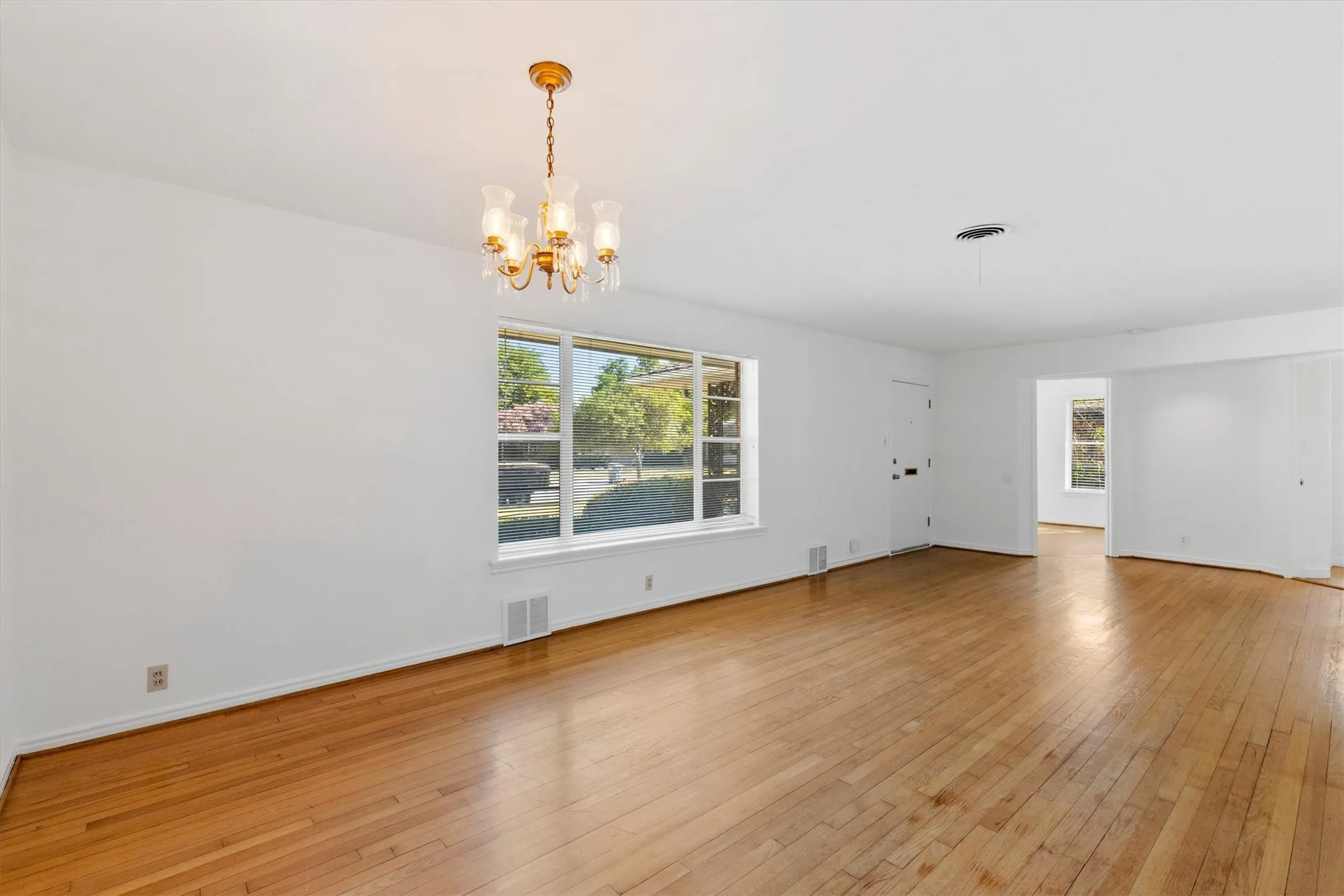 Hardwood flooring, large picture window, and a decorative chandelier