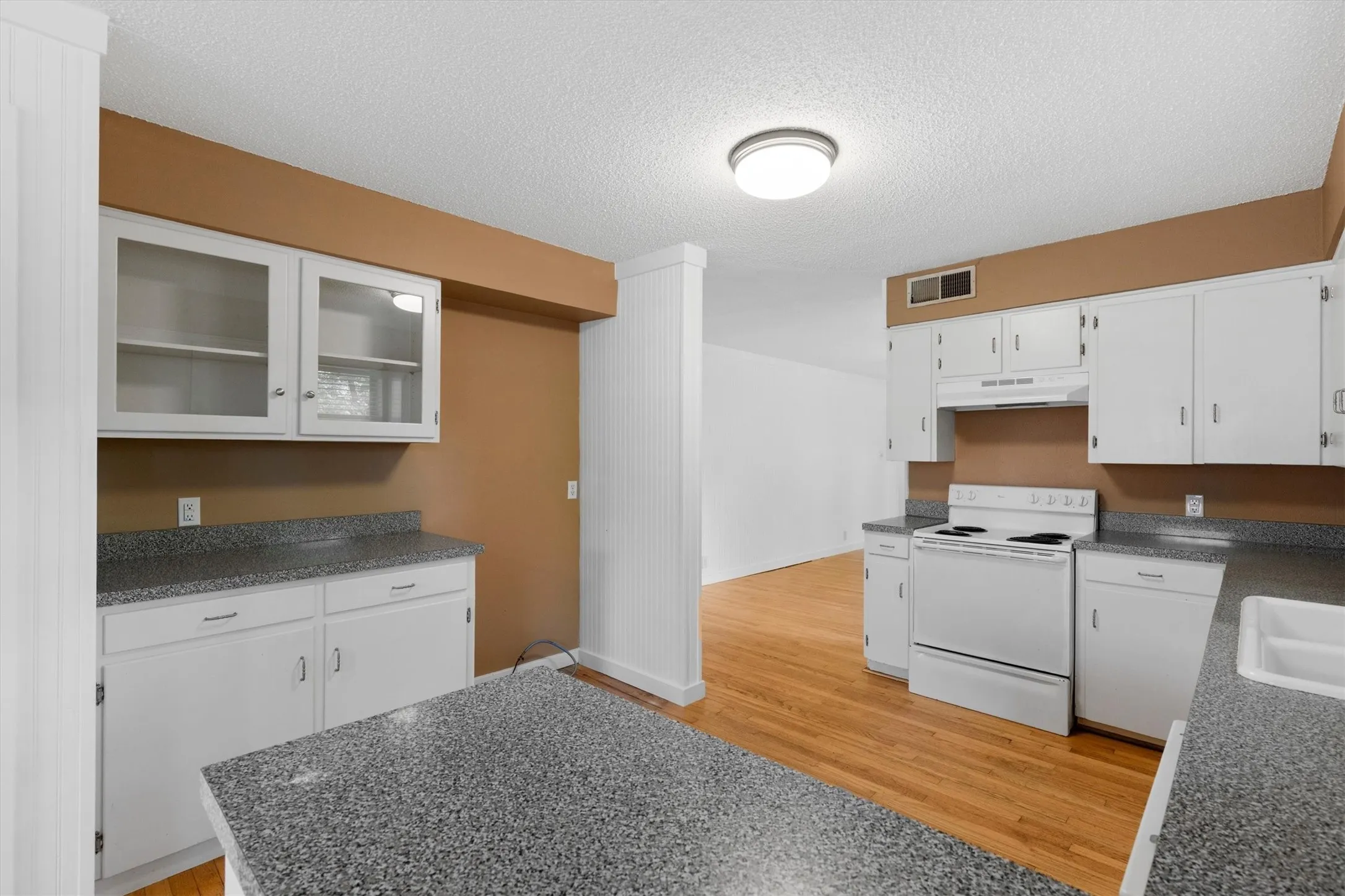 White cabinetry, grey speckled countertops, white appliances, wood-finish flooring, and a ceiling-mounted light fixture