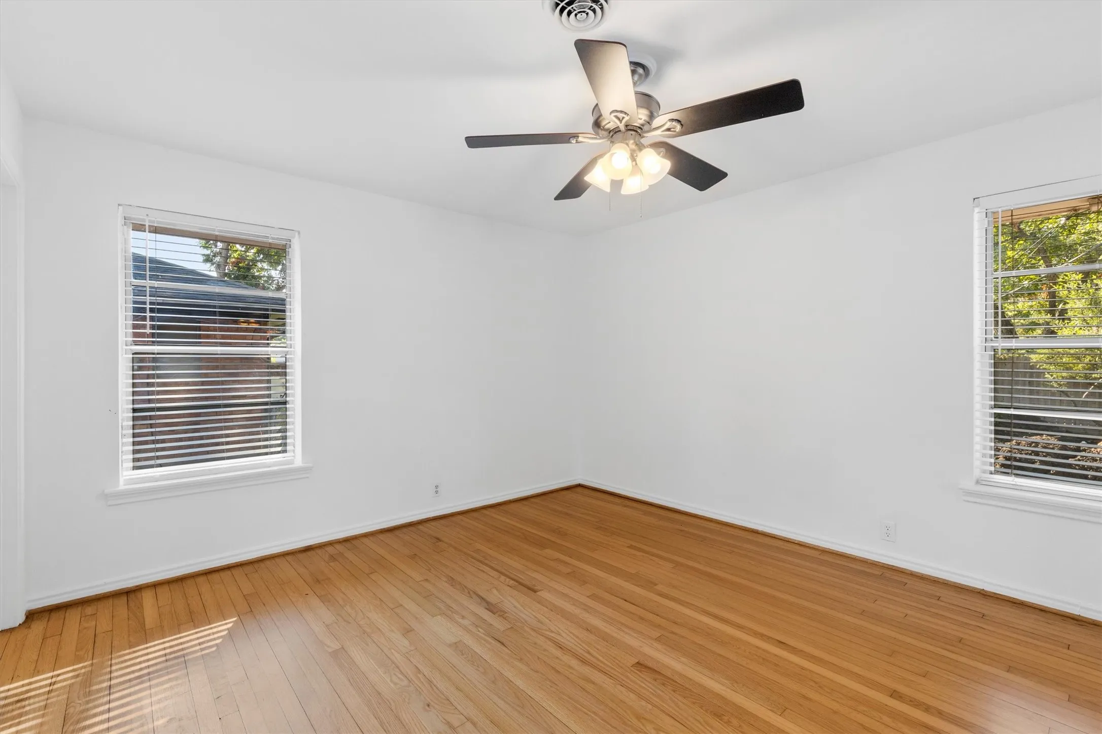 Hardwood flooring throughout, two windows with blinds, and a ceiling fan with integrated lighting