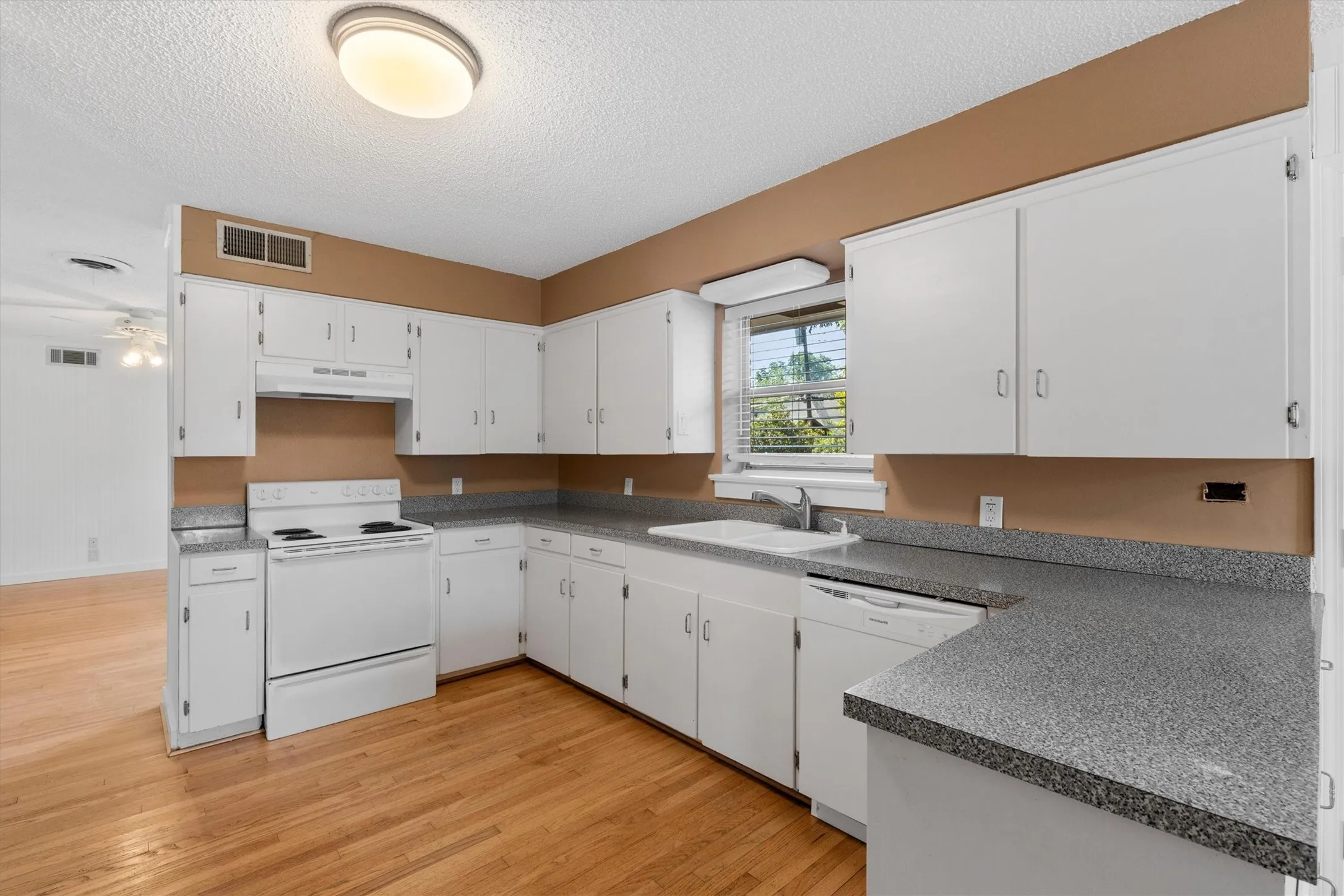 Kitchen featuring white cabinetry, gray speckled countertops, white appliances, a window with blinds, and wood-finish flooring