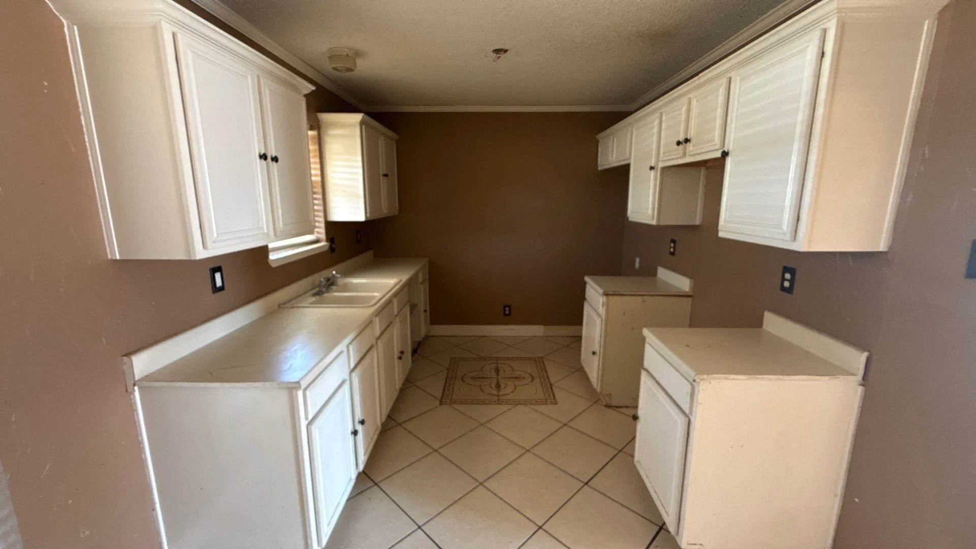 White cabinetry with black hardware, double basin sink, light-toned countertops, and ceramic tile flooring