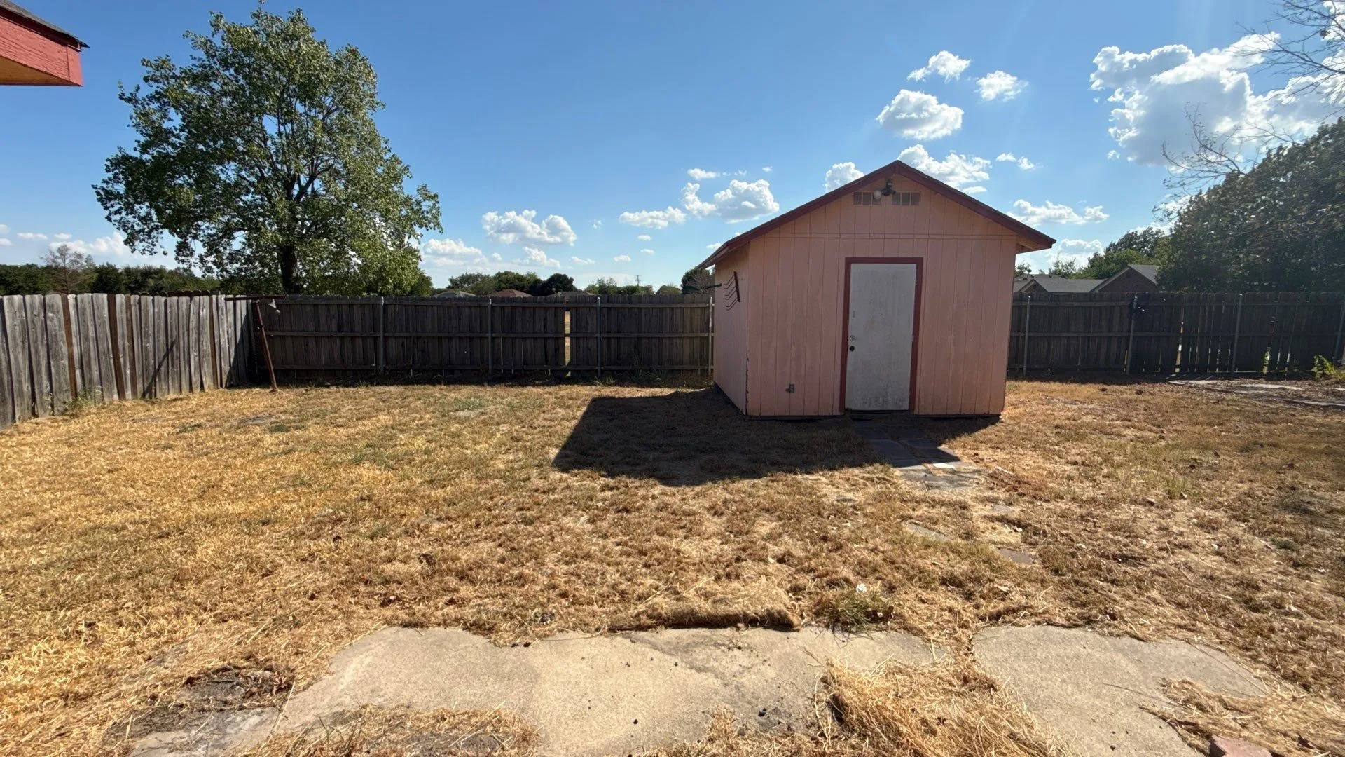 Backyard featuring a privacy fence, mature trees, and a detached shed with a gabled roof