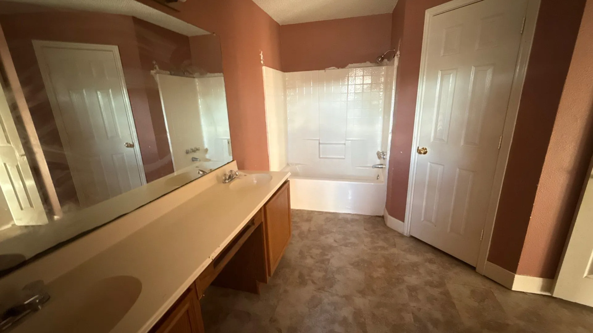 Vanity with integrated sink, expansive mirror, wood-finish cabinetry, and a full bathtub with tiled surround