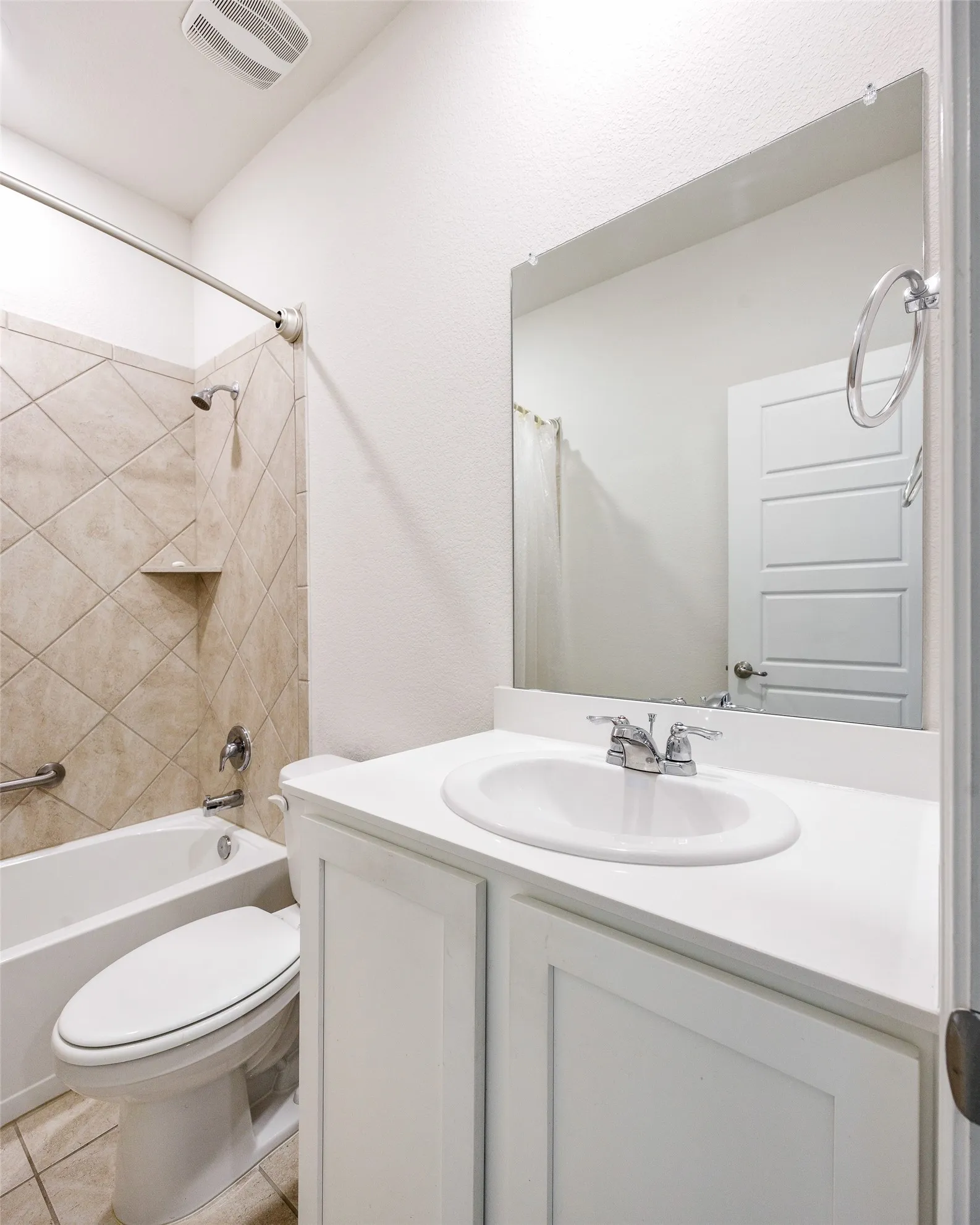 Bathroom featuring a white vanity with an integrated sink, polished chrome fixtures, a tiled tub-shower combination with a built-in shelf, and a wall-mounted mirror