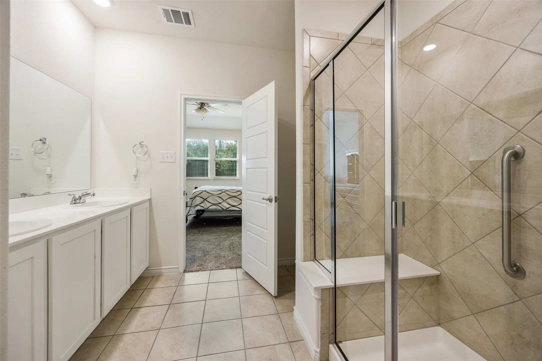 Double vanity with undermount sinks, tile flooring, glass-enclosed shower, and a built-in shower bench