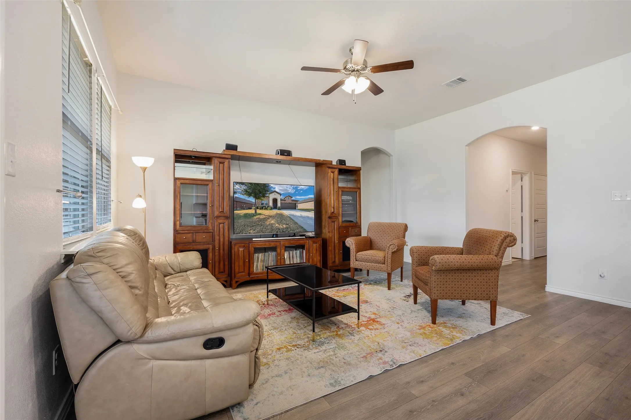Spacious living area featuring wood-finish flooring, high ceilings, and a ceiling fan