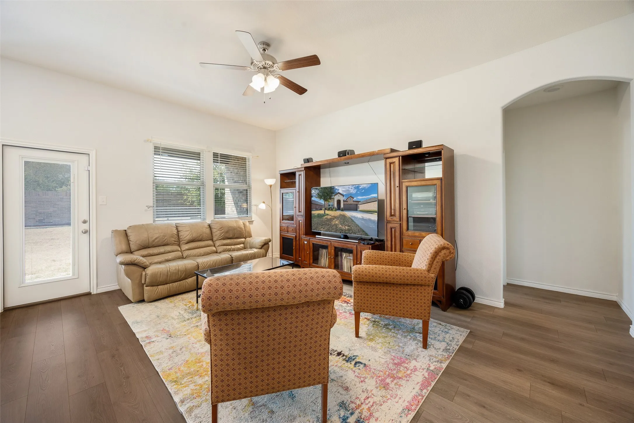 Vaulted ceiling with a ceiling fan, wood-finish flooring, two windows with blinds, glass-paneled exterior door, and an arched entryway