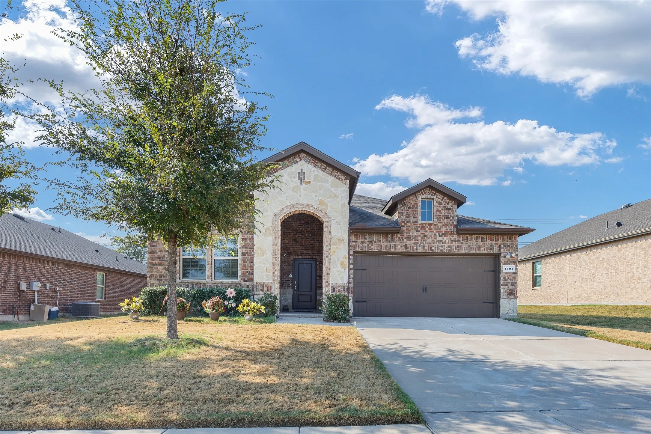 Brick and stone façade, arched entry, dormer window, attached garage, concrete driveway