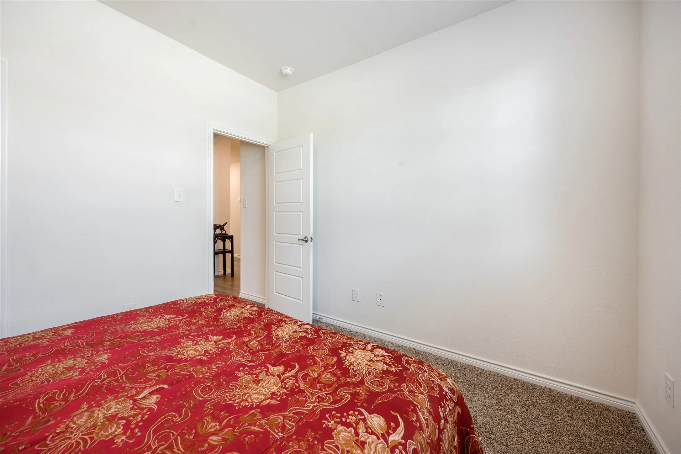 Spacious bedroom with neutral white walls, neutral carpeting, and ceiling fixtures