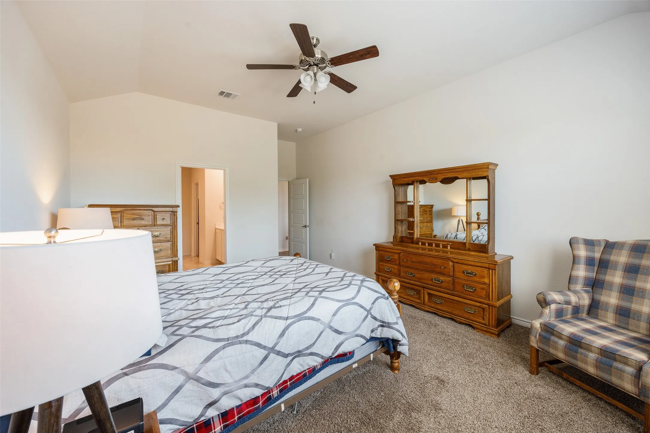 Vaulted ceiling with a ceiling fan, carpeted flooring, and a doorway leading to an additional space
