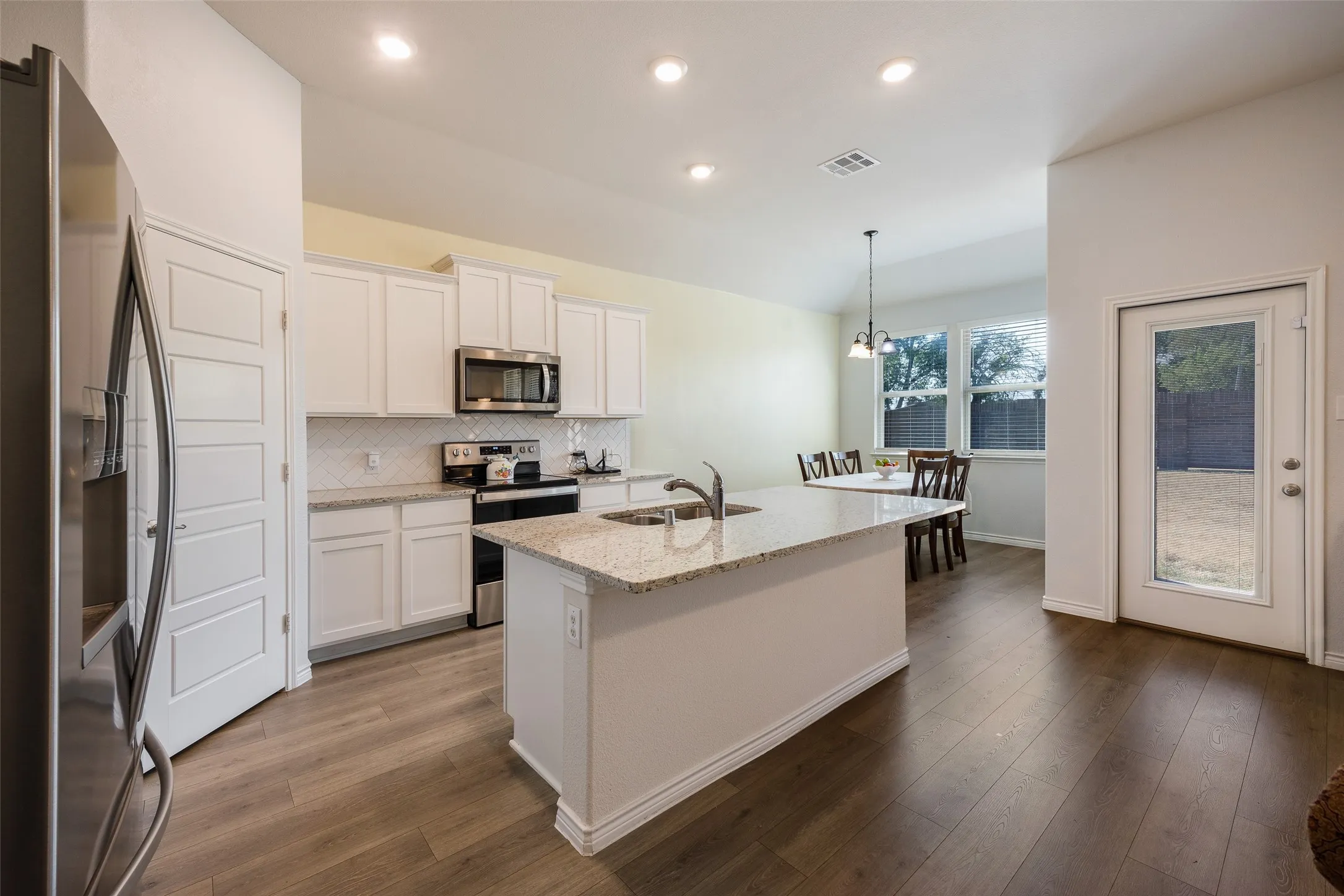 Kitchen featuring white cabinetry, stainless steel appliances, a center island with a sink, and wood-finish flooring