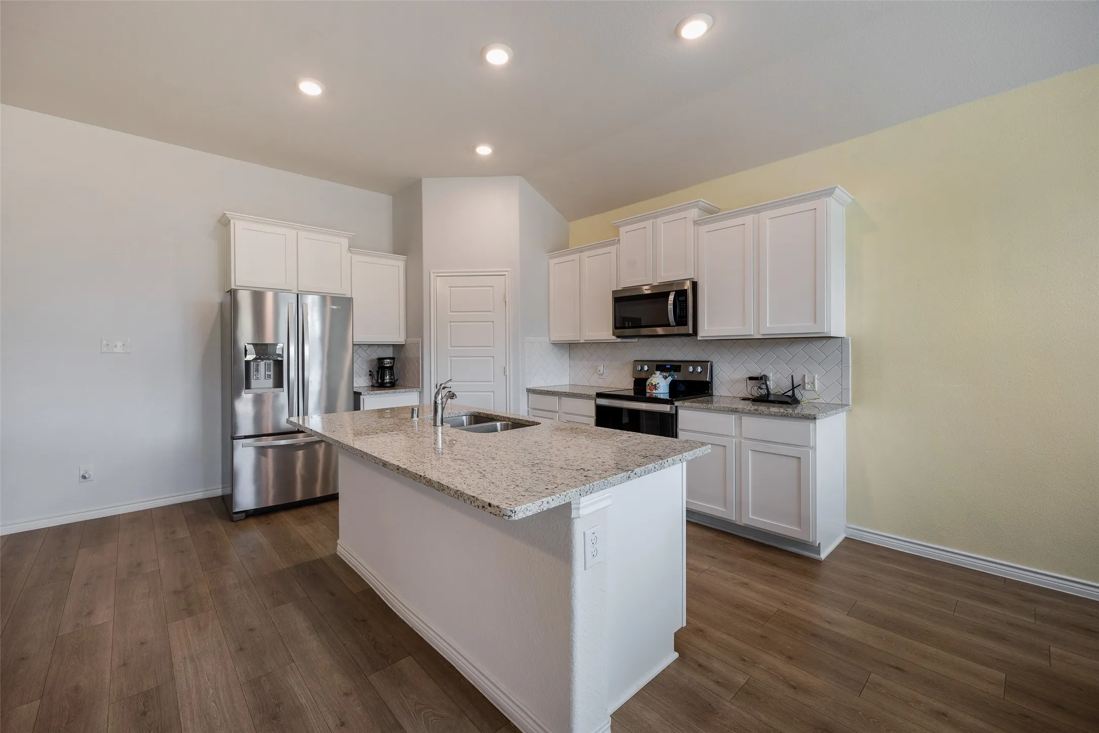 Kitchen featuring wood-finish flooring, recessed lighting, white cabinetry, a kitchen island with sink, and stainless steel appliances