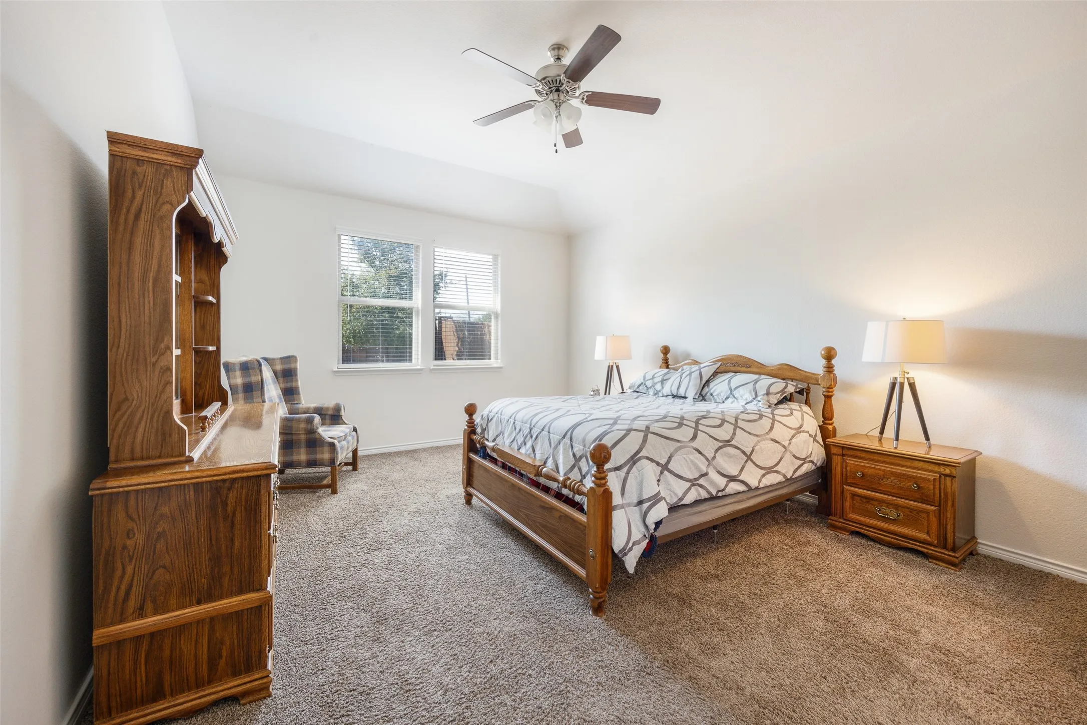 Vaulted ceiling with a ceiling fan, dual windows with blinds, and neutral carpet flooring