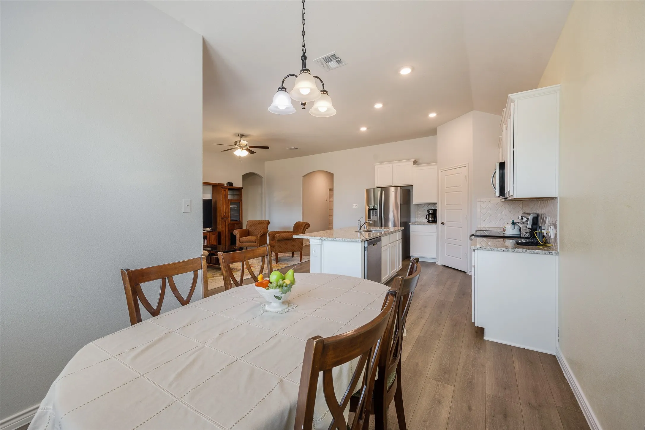 Open-concept living space featuring wood-finish flooring, recessed lighting, white cabinetry, and a kitchen island with stone countertops