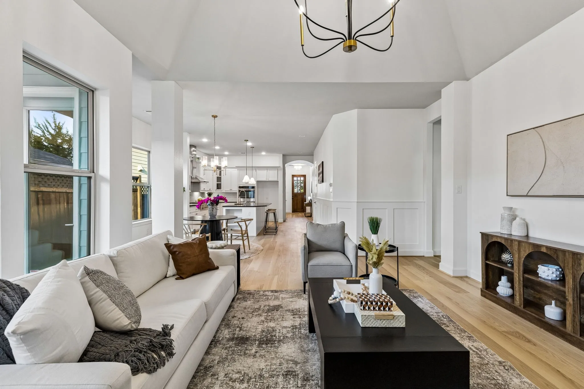 Vaulted ceiling with modern chandelier, light wood-finish flooring, white paneled wall accents and recessed lighting