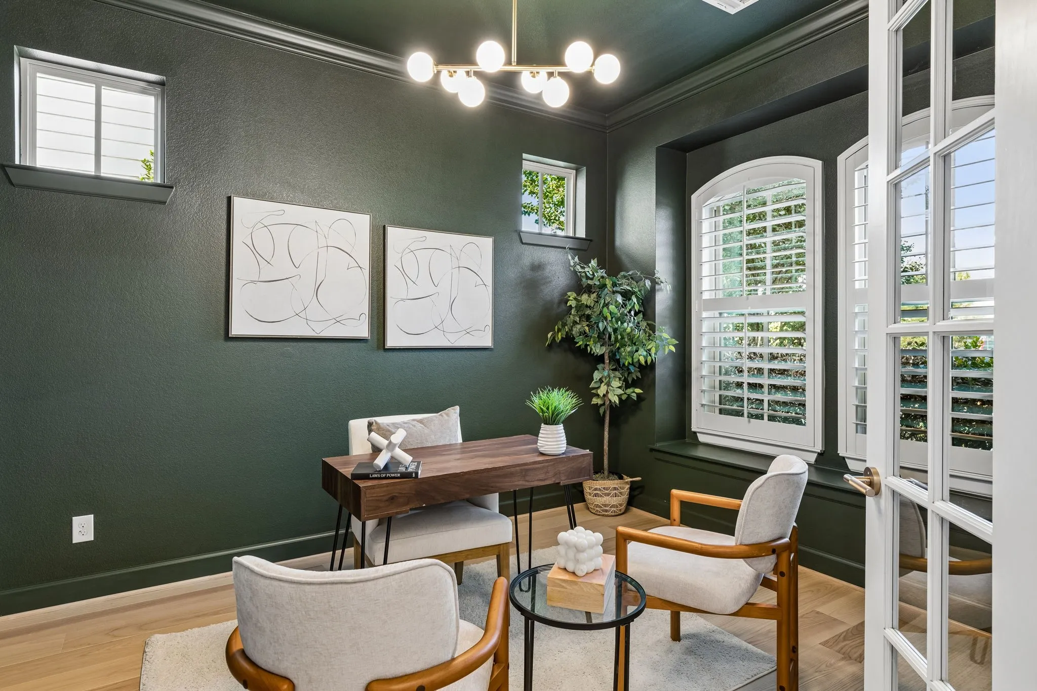 Dark green walls with crown molding, light wood-finish flooring, French doors with glass panes, transom windows, and arched windows with plantation shutters