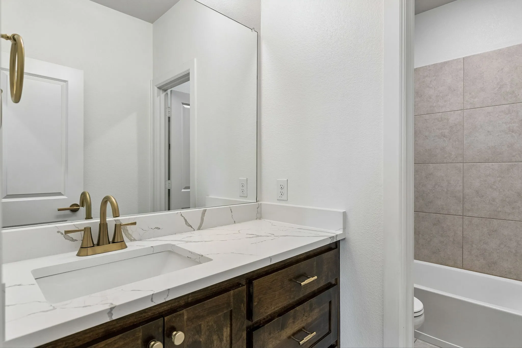 White vanity with a quartz countertop, integrated rectangular sink, and champagne bronze-finish fixtures