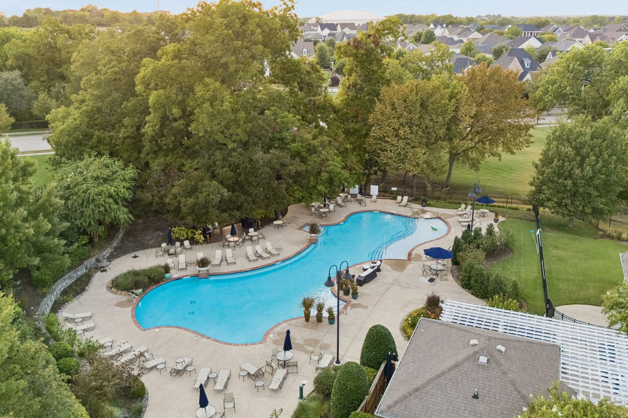 Resort-style pool with integrated steps, surrounding concrete patio, lounge chairs, and umbrella-shaded tables