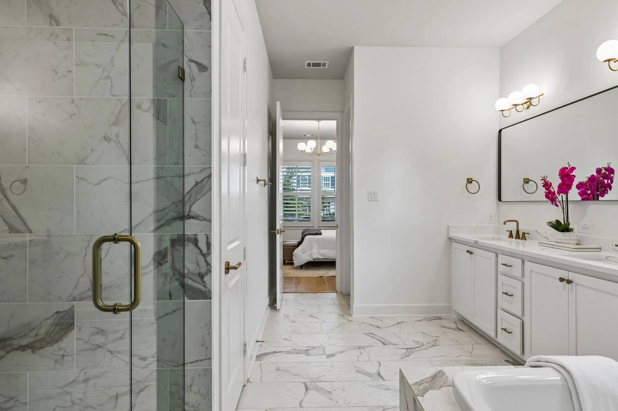 Spacious bathroom featuring a frameless glass shower enclosure, a dual quartz vanity with white cabinetry, a large rectangular mirror, and marble-look tile flooring