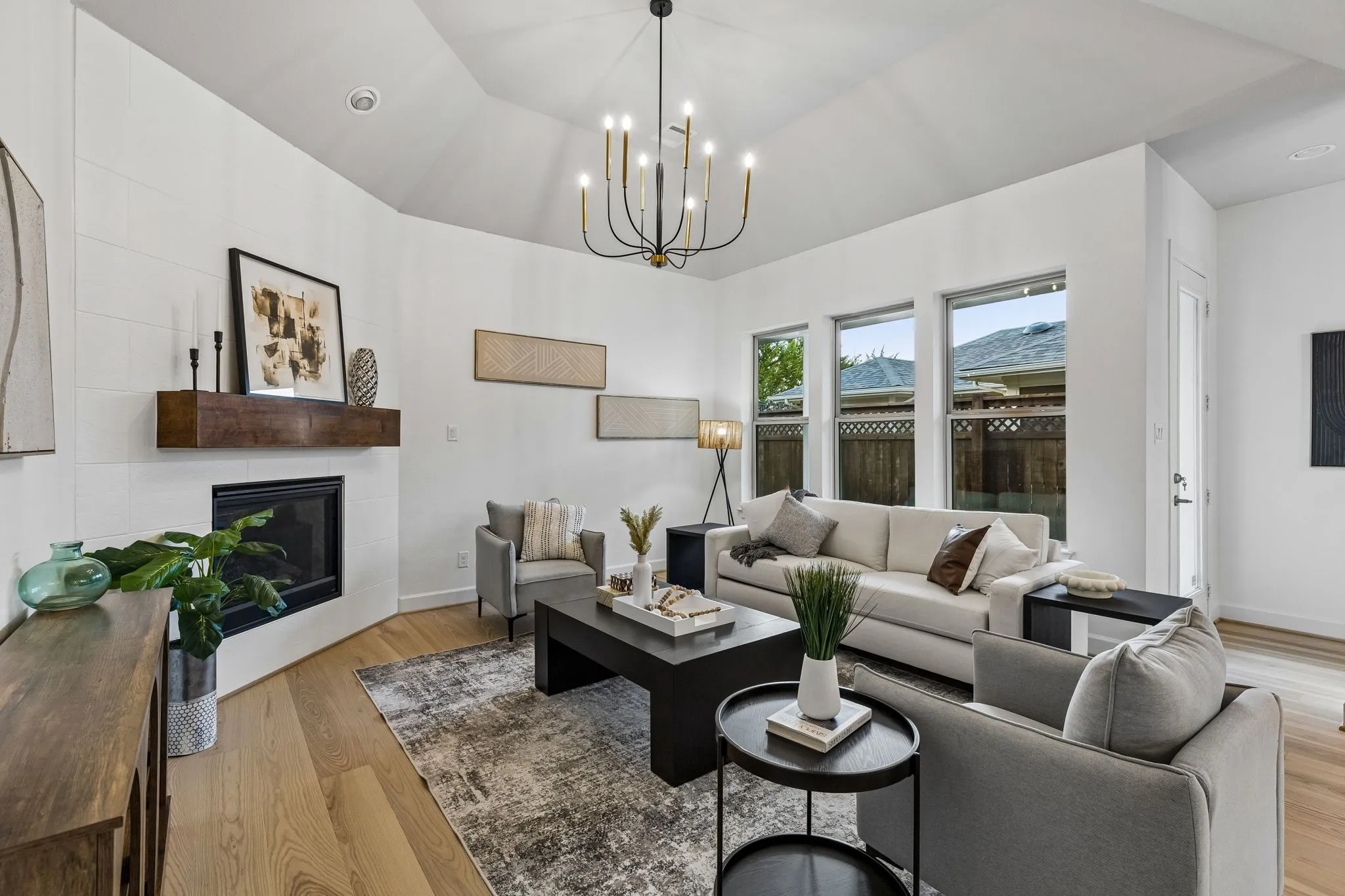 Vaulted ceiling with an elegant chandelier, a corner fireplace featuring a substantial wood mantel, white oak flooring