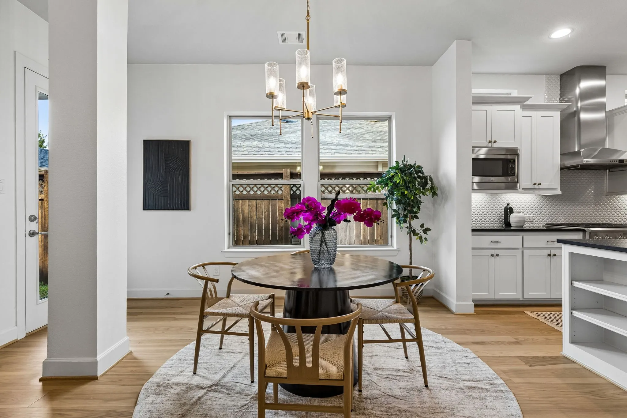 Open concept living space featuring wood-finish flooring, a modern chandelier, and a kitchen with white cabinetry, stainless steel appliances, and a textured backsplash