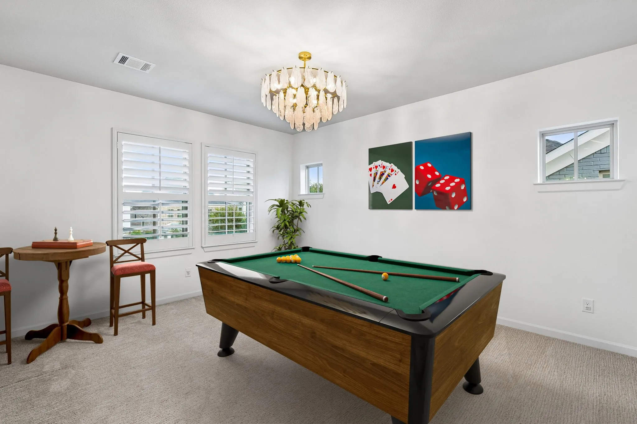 Carpeted room featuring a pool table, multiple windows with white plantation shutters, and a decorative chandelier