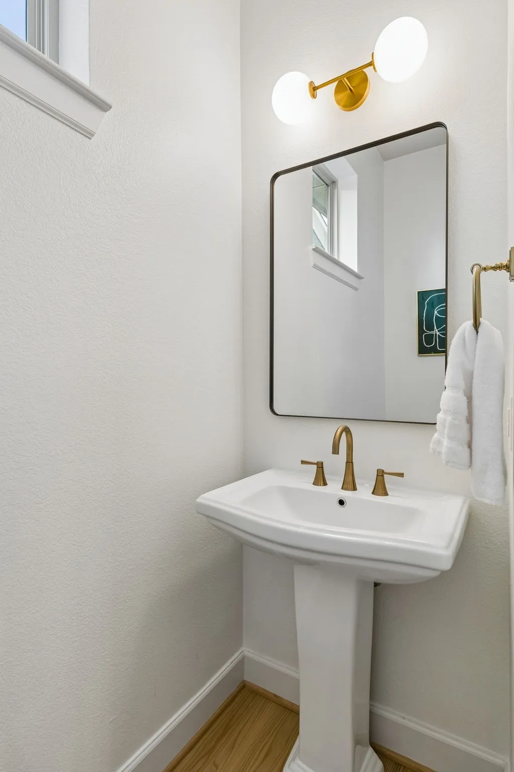 Pedestal sink with champagne bronze-finish faucet, rectangular framed mirror, and two-light vanity fixture