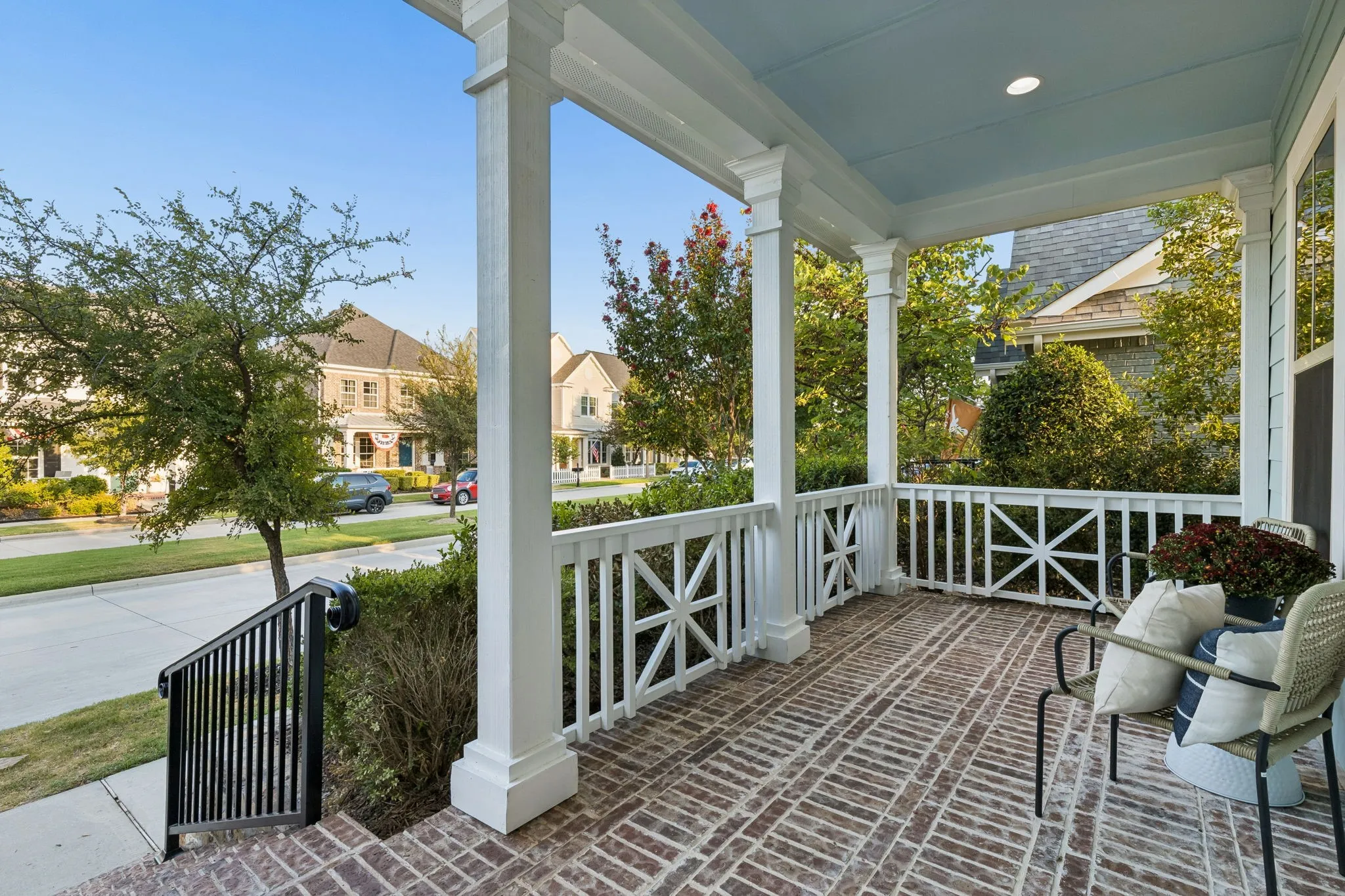 Brick-patterned porch flooring, white column supports, classic railing design, light-colored ceiling, and recessed lighting