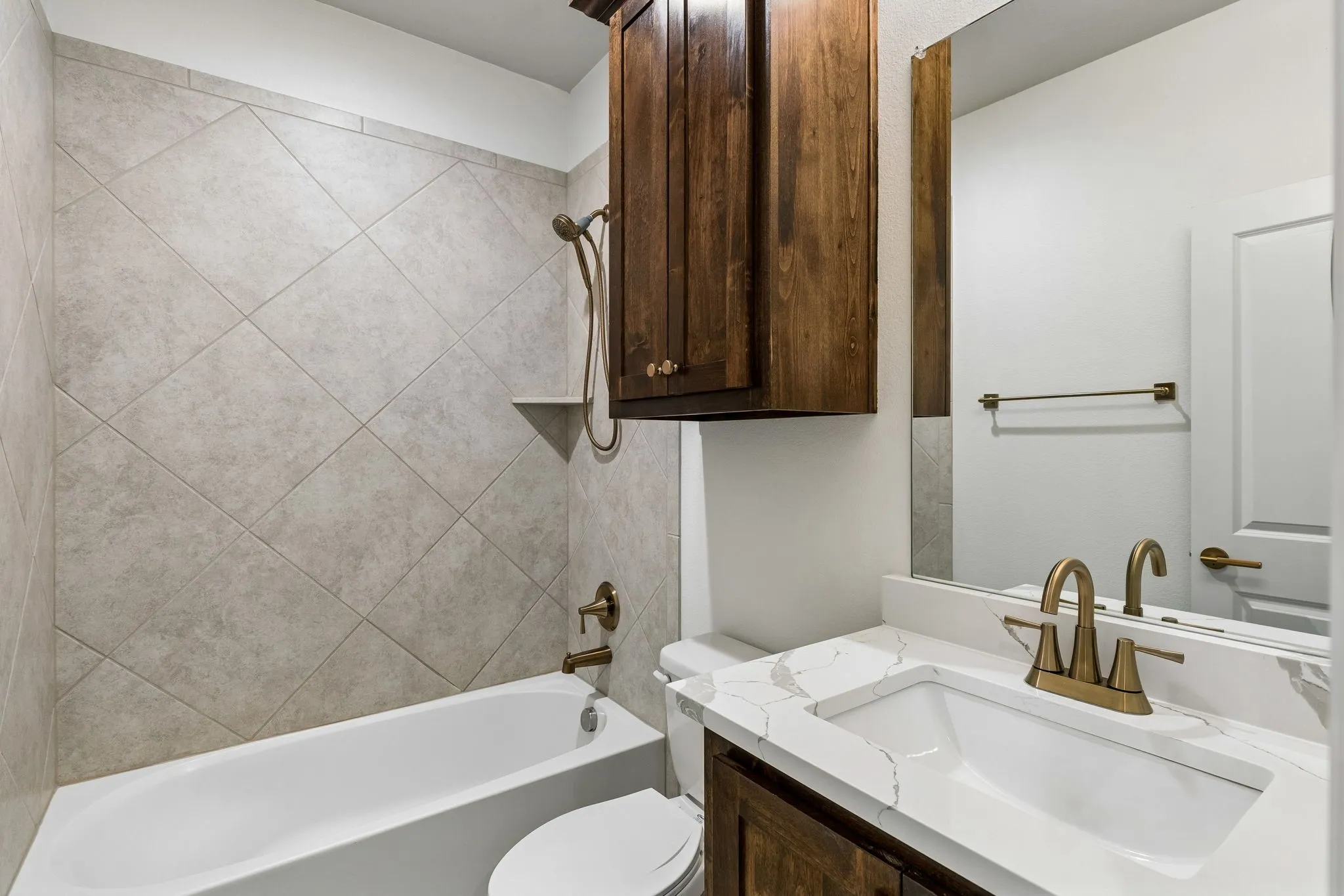Bathroom featuring a white tub, diagonal tile surround, built-in shower shelf, a vanity with updated quartz countertop, and dark wood-finish cabinet