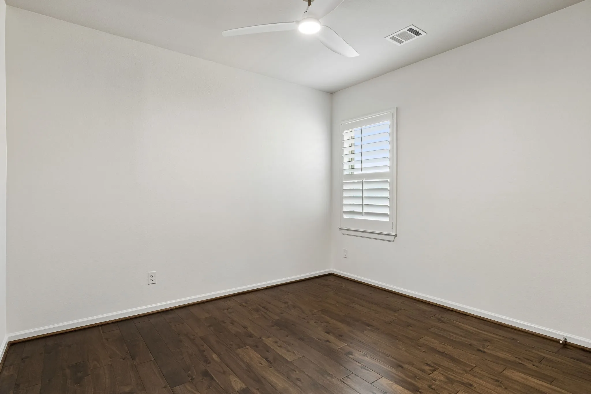 Wood-finish flooring, white walls, and a window with white plantation shutters