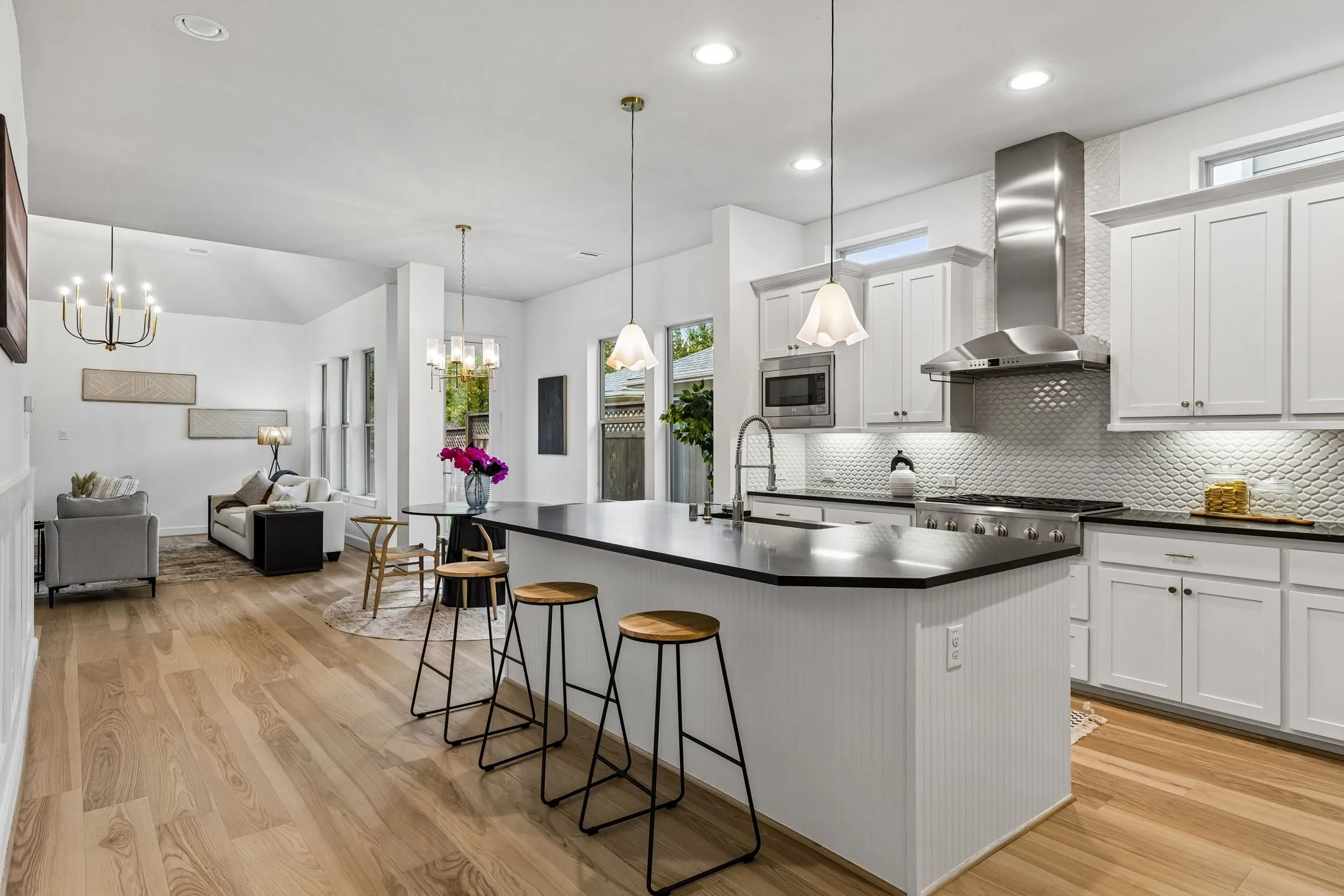 Open-concept layout with white oak hardwood flooring, a kitchen island, white cabinetry, and stainless steel appliances